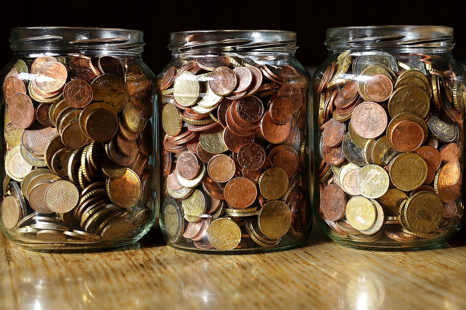 Drei nebeneinander stehende Gläser gefüllt mit Cent- und Euro-Münzen